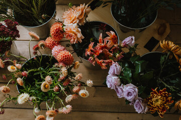 A vibrant collection of various colorful flowers arranged in metal buckets on a wooden floor,...