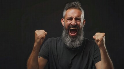 Obraz premium Expressive man celebrating success with a joyful scream in a dark setting while raising his fists in excitement