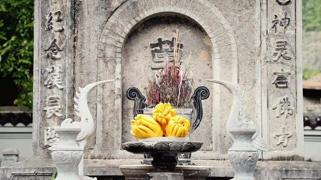upward pan shot of an ancient stone altar at Thai Vi Temple in Tam Coc Vietnam traditional offerings of Citrus medica var. sarcodactylis also known as Buddha's hand or fingered citron burning incense