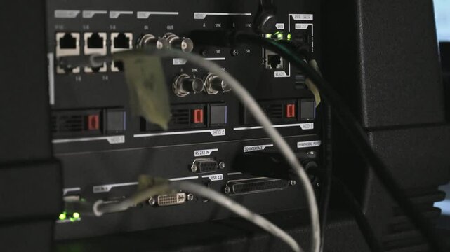 The clip is about a cinema projector interface. It is turned on and has some cables connected to it. The lights for the storage drives are also blinking. It is a laser projector.