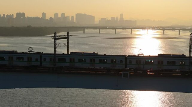 A subway train crossing Dangsan Bridge in Seoul against a backdrop of a reddish-yellow sunrise