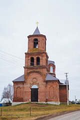 Fototapeta premium The historic red brick church, featuring a beautiful bell tower, is gracefully set amidst the surrounding nature, creating a picturesque scene