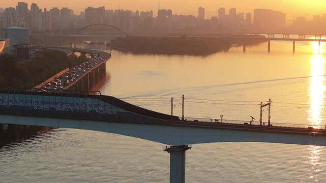A subway train crossing Dangsan Bridge in Seoul against a backdrop of a reddish-yellow sunrise