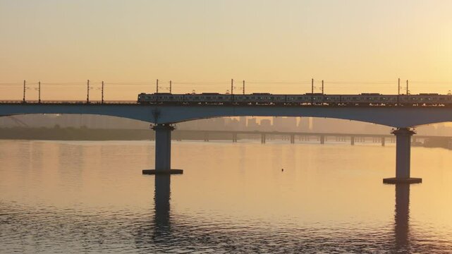 A subway train crossing Dangsan Bridge in Seoul against a backdrop of a reddish-yellow sunrise