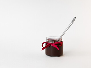 Small glass jar of chocolate spread with red ribbon and spoon on white background