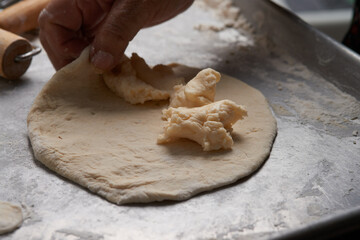 Close-up of an elderly woman's hands preparing cheese-filled panzerotto in a rustic pan, highlighting traditional cooking techniques.