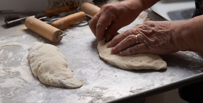 Close-up of an elderly woman's hands preparing cheese-filled panzerotto in a rustic pan, highlighting traditional cooking techniques.