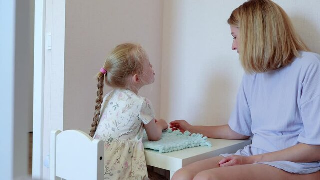 Mother and daughter are seen engaging in shared craft project bonding through art of handiwork. Mom and child are shown working oa craft project in their home enjoying peacefulness of doing things.