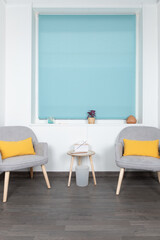 White living room with two gray armchairs, yellow cushions, blue blind and minimalist decoration. Interior concept and minimalist decoration
