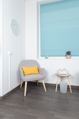Corner of a living room with a gray armchair, yellow cushion, blue blind and minimalist decor. Interior concept and minimalist decoration