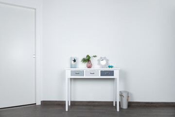White table with 3 gray drawers with table lamp, white mirror and vase with decorative plant with white background wall and door. Interior concept and minimalist decoration
