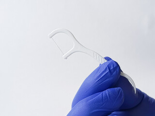 Dental floss with plastic handle on white background. Dentist's hand in blue medical glove holds flosser close-up.