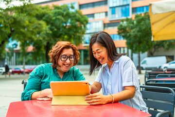 Disabled woman and friend using tablet sitting on sidewalk cafeteria