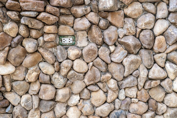 Ancient stone wall texture background and there is a white power outlet.