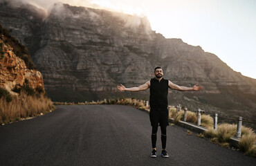 Fitness, man and open arms for freedom, relax or exercise for body health on road by mountains. Outstretched, happy runner and outdoor for sports, peace or breathing fresh air for wellness or success