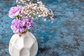 Bouquet of spring flowers in a porcelain white vase on blue background.