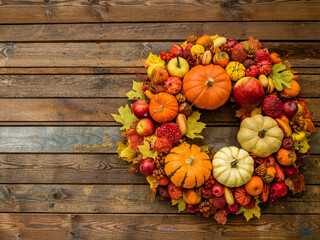 Colorful autumn wreath with pumpkins, fruits and leaves on wooden background. Place for text