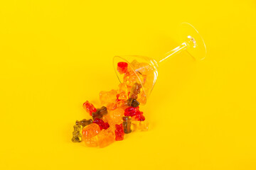 Fruit flavored worm shape, jelly candies in a glass on yellow background.