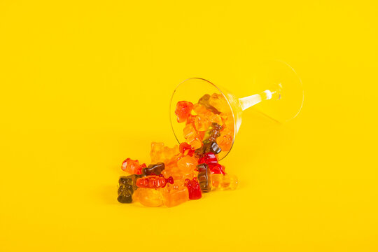 Fruit flavored worm shape, jelly candies in a glass on yellow background.