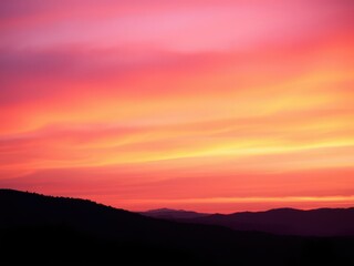 Vibrant orange, pink and purple hues blending into a serene gradient over a silhouetted landscape, background