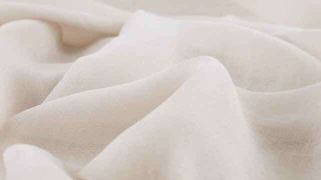 Close-up view of the soft folds of thin white color chiffon fabric on a rotating display case. Textile background with sewing accessories on the theme of fashion, design, fabrics, shades of color.
