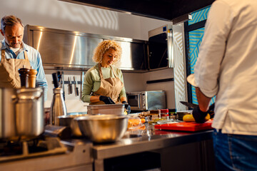 Middle-aged couple enjoying a cooking class with a chef preparing zucchini for a meal in the kitchen.