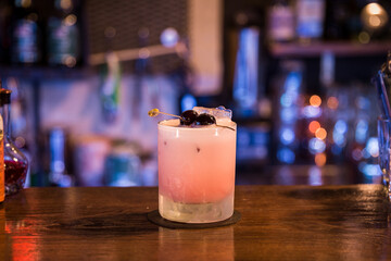 A cocktail stands on a wooden table in the background colorful lights can be seen