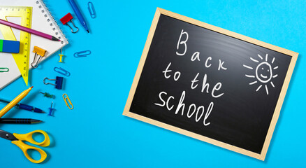 Back to school stationery arrangement with colorful supplies and a chalkboard message on a blue background