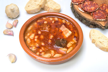 Clay casserole with Asturian fabada, surrounded by traditional ingredients such as garlic, bread and sausages. Typical dish of Spanish cuisine, ideal for gastronomy and traditional recipes
