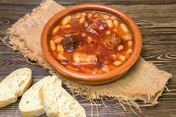 Clay casserole with Asturian fabada, surrounded by traditional ingredients such as garlic, bread and sausages. Typical dish of Spanish cuisine, ideal for gastronomy and traditional recipes