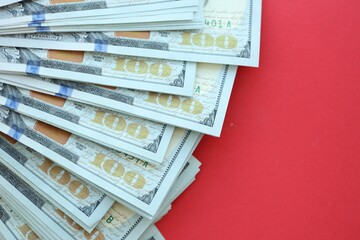 Big amount of hundred dollar bills in thick stack lies on bright red color paper background
