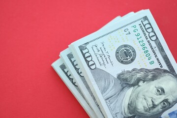 Big amount of hundred dollar bills in thick stack lies on bright red color paper background