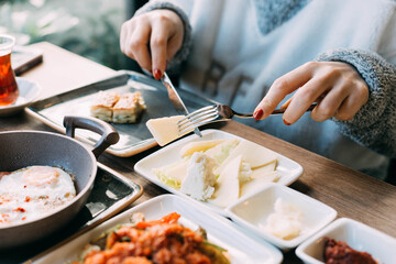 Woman enjoying a traditional Turkish breakfast with assorted dishes like cheese, olives, tomatoes, cucumbers, and tea, capturing the richness and warmth of Turkish morning rituals and flavors.