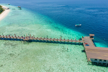 Aerial view of a wooden pier extending into clear turquoise waters with a boat and sun loungers on...