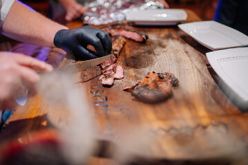 Obraz premium A chef slices grilled steak on a wooden board, preparing to serve on white plates. The steak is charred and juicy, with engraved details visible on the board..