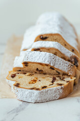 Traditional German Christmas cake Stollen sliced into pieces with raisins, fruits and nuts inside and sprinkled with powdered sugar on the white background