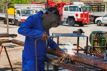 welder working outdoors, african worker welding a pipe in the yard