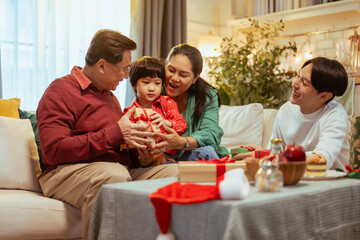 parent, relaxation, celebrating, enjoying, present, gift, children, christmas, parenting, surprise. A family is sitting on a couch and one of the children is holding a red present.