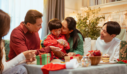 parenthood, kid, party, celebrating, enjoying, happy, celebrate, present, childhood, christmas. A family is gathered around a table. The child is holding a present and the family is enjoying.