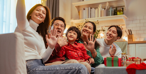 parent, parenthood, sofa, couch, enjoyment, waving, selfie, group, friendship, family. A family of five is sitting on a couch, smiling and waving at the camera. Scene is warm and joyful.