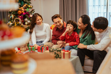 presents, happiness, family, enjoying, gifts, xmas, present, festive, celebration, christmas. A family of four is sitting on a couch in front of a Christmas tree.