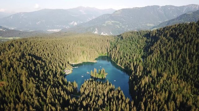 Wide drone shot of the stunning Cauma Lake nestled amidst a dense forest and majestic mountains in Graub&uuml;nden, Switzerland