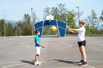 Fototapeta premium Mother and son playing basketball outdoors on sunny day