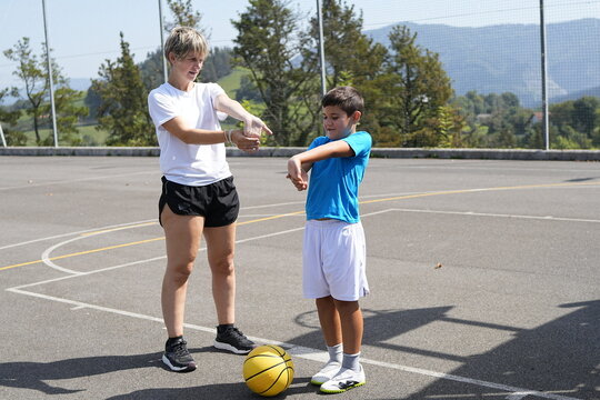 Coach stretching arms with young basketball player on outdoor court