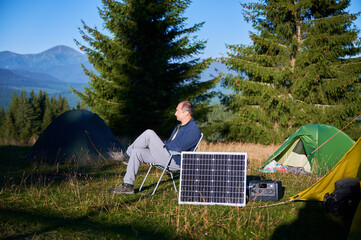 Man using photovoltaic solar panel for charging portable power station outdoor in eco-friendly...