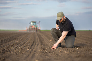 Farmer examing dirt while tractor is sowing field