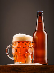 A bottle of beer and a glass of beer on a dark background.