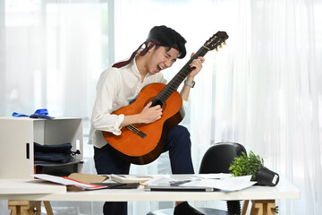 Fototapeta premium Joyful employee playing guitar during break at the workplace