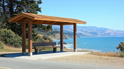 Simple wooden bus stop along a coastal road, with ocean waves in the background under clear skies.