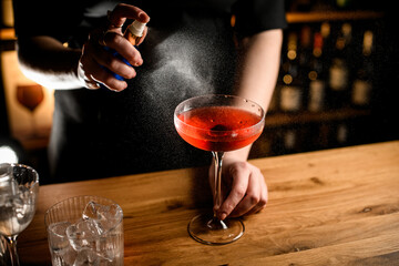 Female bartender sprays a glass from a blue spray bottle standing on a bar counter